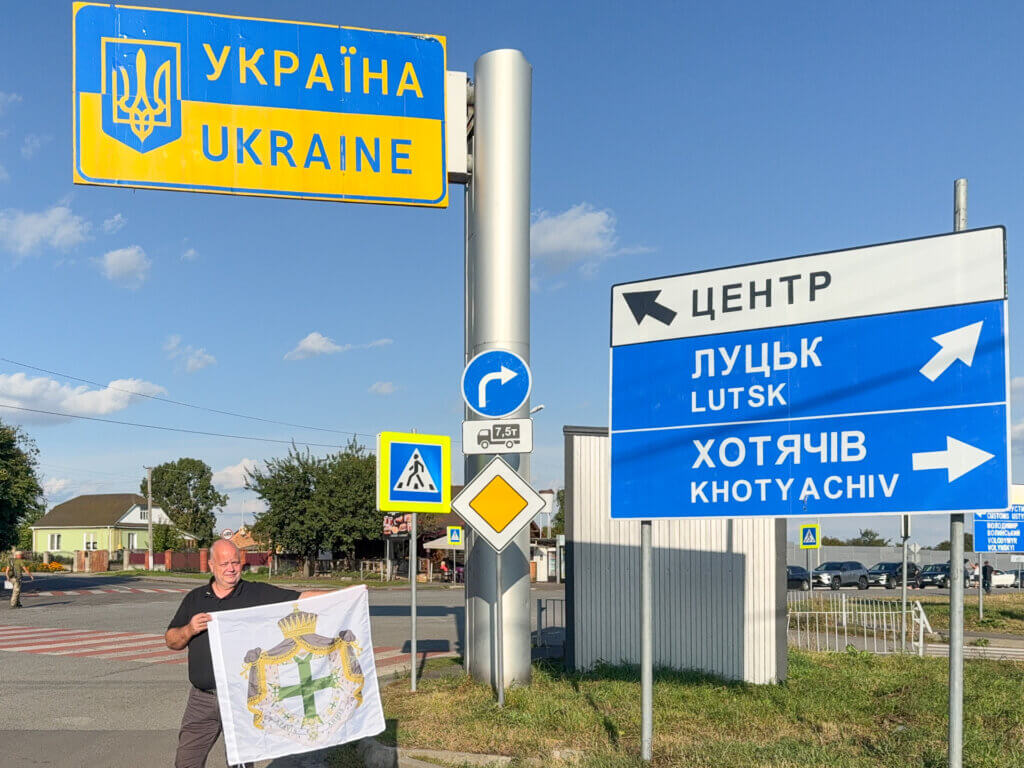 Lazarus-Teammitglied mit Fahne des Lazarus-Ordens unter dem Schild „Ukraine“ nach der erfolgreichen Einreise