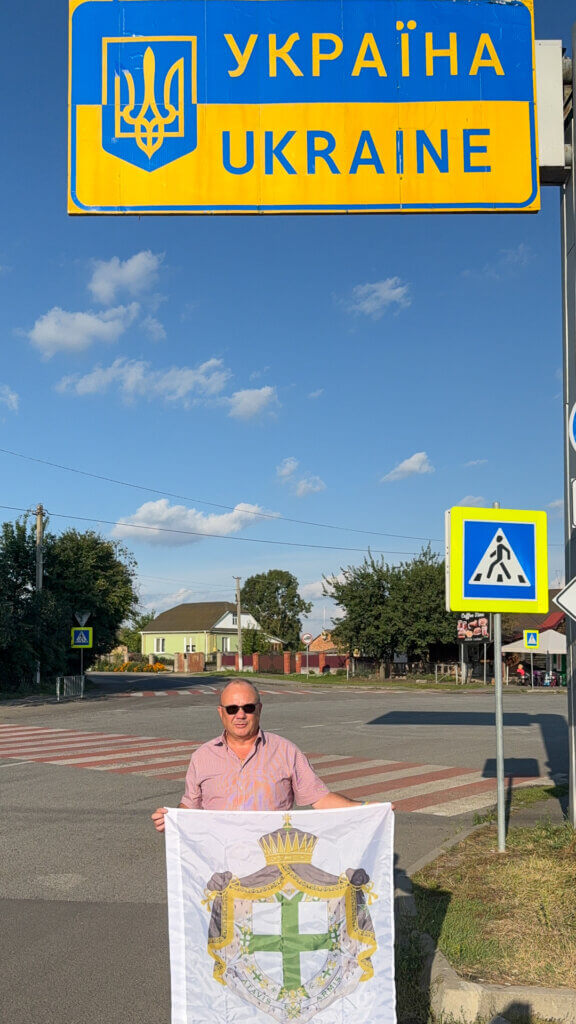 Lazarus-Teammitglied mit Fahne des Lazarus-Ordens unter dem Schild „Ukraine“ nach der erfolgreichen Einreise